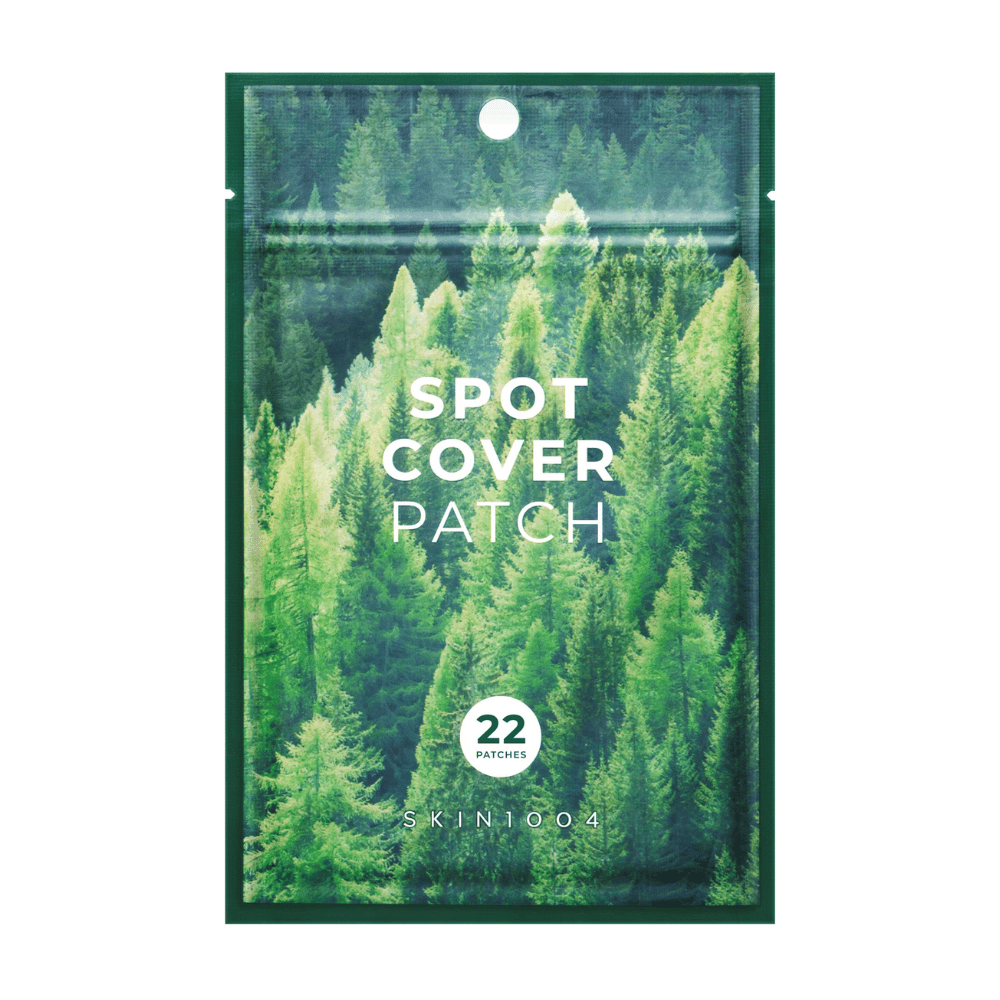 Empaque con "Spot Cover Patch" que contiene 22 parches, diseñado con un motivo de bosque verde. El texto "SPOT COVER PATCH" está impreso en blanco en la parte delantera, y un círculo marca la cantidad de parches. El producto es de la marca SKIN1004.