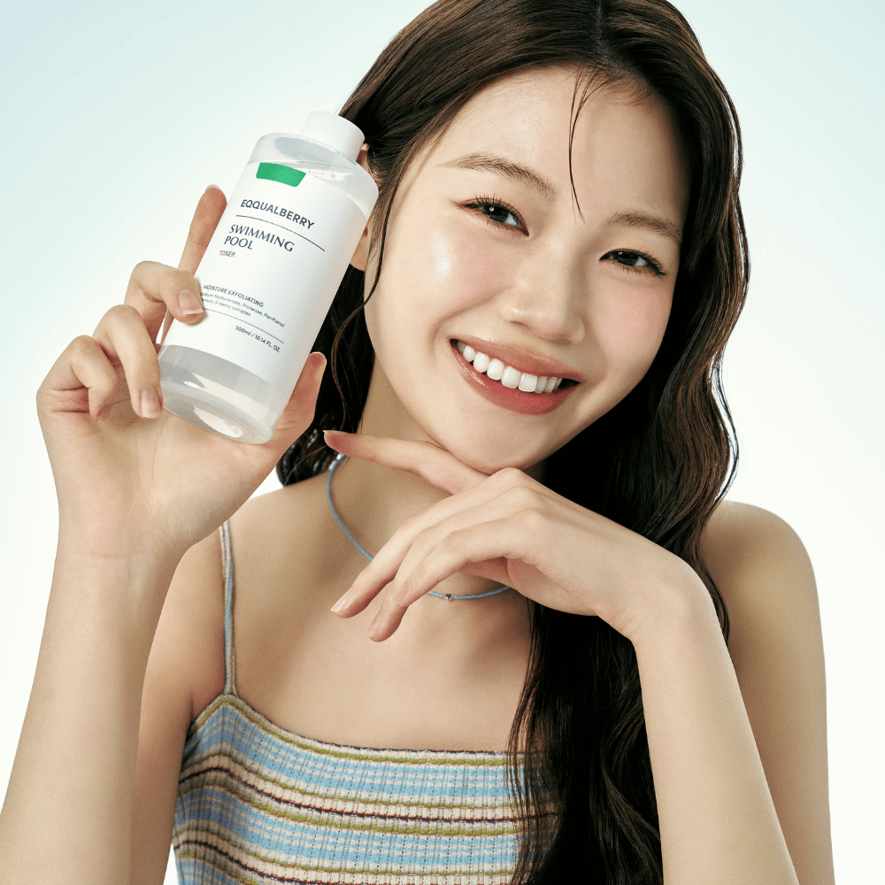 Mujer sonriente con piel radiante sostiene Equalberry Swimming Pool Toner. Look fresco y natural con maquillaje ligero y un atuendo veraniego en tonos azules.