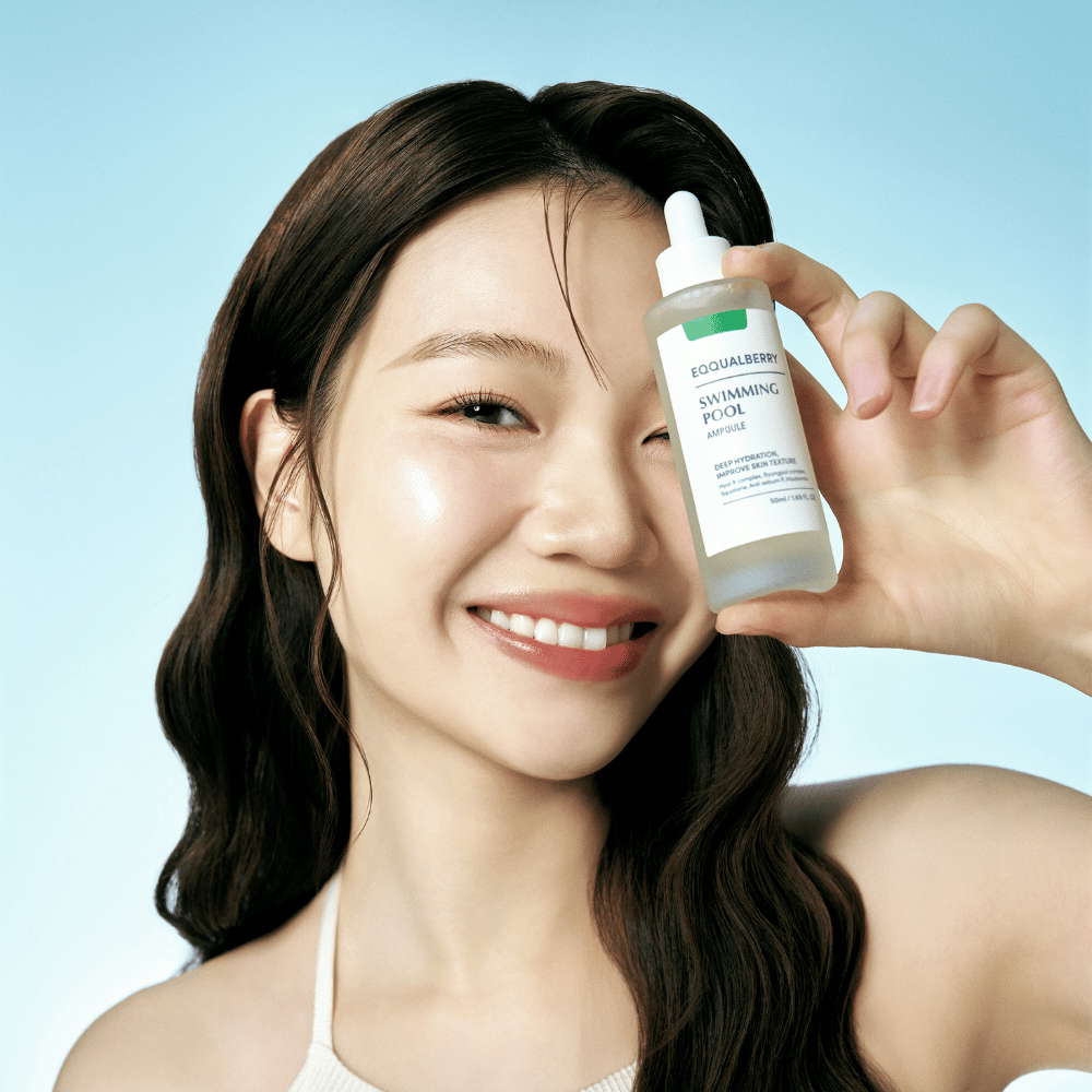 Una mujer sonriente sostiene Eqqualberry Swimming Pool Ampoule, un producto para el cuidado de la piel para hidratación intensa, frente a un fondo azul claro.