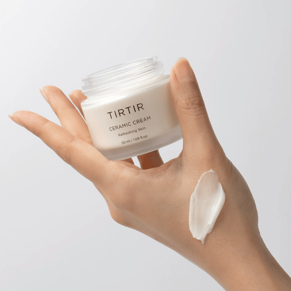 Una mano sostiene un tarro con TIRTIR Ceramic Cream. En el dorso de la mano se ha aplicado una cantidad de la crema. La crema parece ser espesa e hidratante. El empaque indica que el contenido es para "Refreshing Skin" y la cantidad es de 50 ml / 1.69 fl oz.
