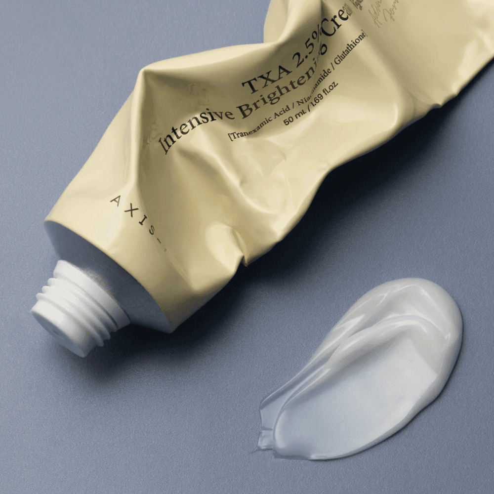 Imagen del producto con el tubo y una pequeña cantidad de crema al lado para mostrar la textura suave y cremosa y la fórmula hidratante. El enfoque está en el brillo y la aplicación uniforme.