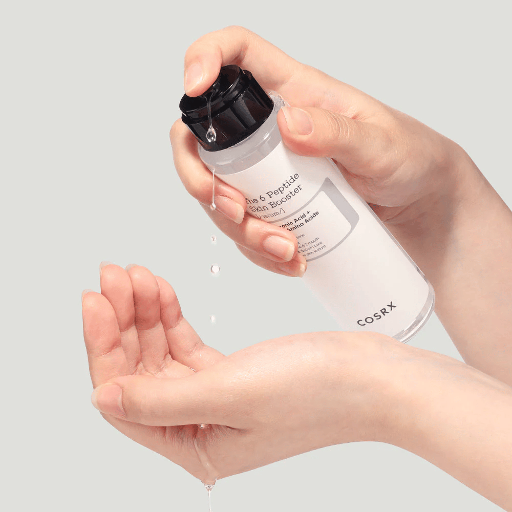 Manos vertiendo producto para el cuidado de la piel de una botella transparente con el texto "The Peptide Skin Booster".