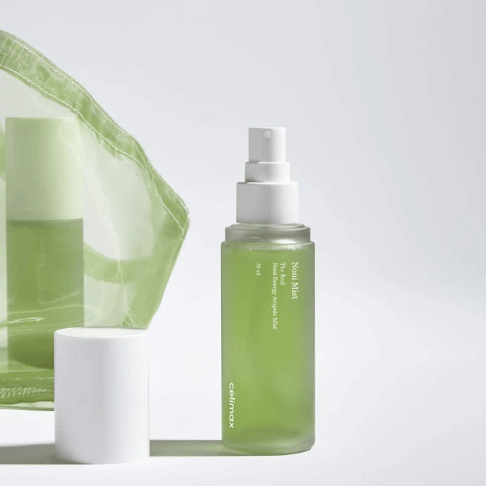 Una botella de Celimax Noni Mist, un frasco pulverizador verde con bomba blanca, que está al lado de una tapa. El producto está empaquetado en una bolsa de plástico transparente y se comercializa como Noni Energy Ampule Mist.