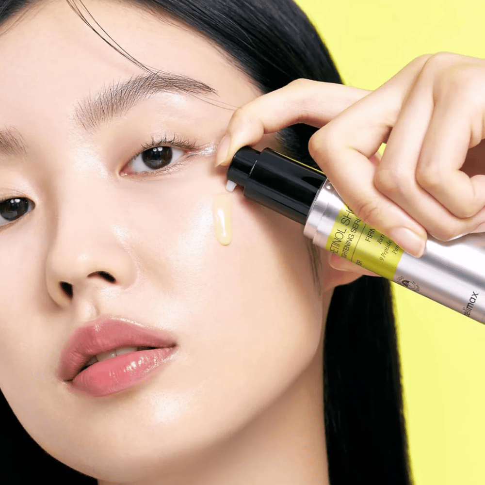 Modelo aplica The Vita-A Retinol Shot Tightening Serum de Tiam cerca del área de los ojos, enfocándose en el brillo de la piel y la consistencia amarilla del suero.
