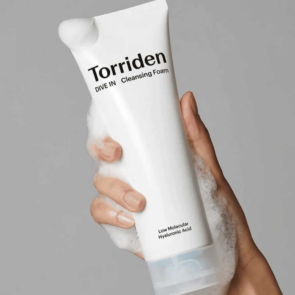 Una mano que sostiene un tubo pH balanceado Torriden DIVE-IN Low Molecular Hyaluronic Acid Cleansing Foam de 150ml.