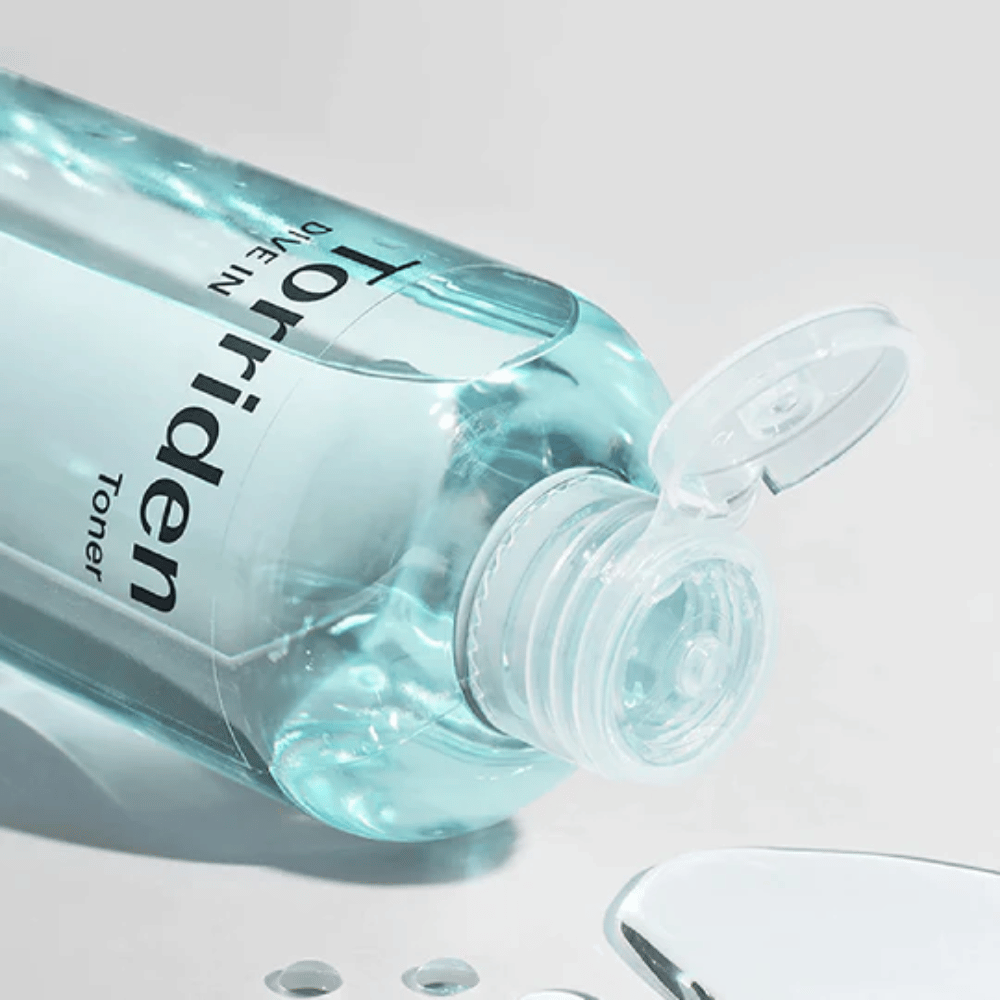 Una botella DIVE-IN Low Molecule Hyaluronic Acid Toner de 300ml al lado de un vaso de agua, promueve Torriden y la hidratación.