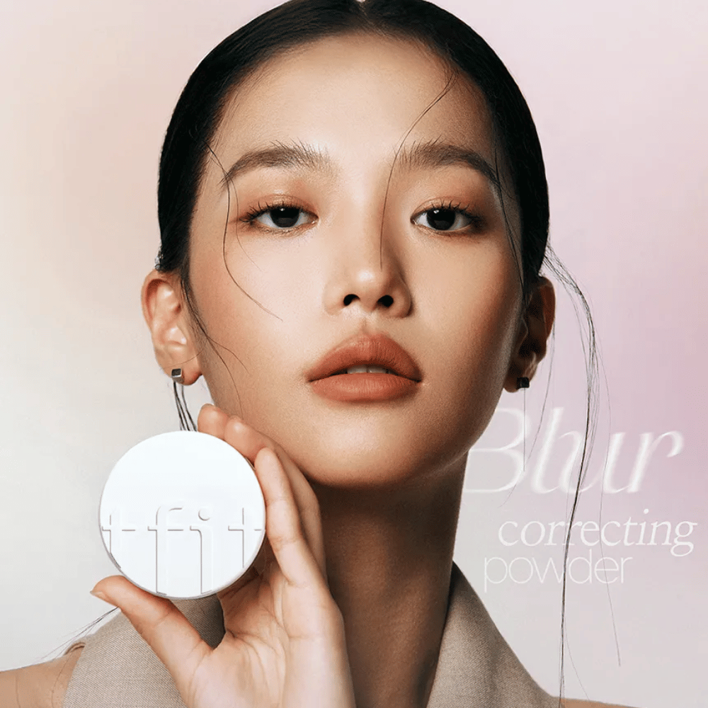 Mujer con maquillaje impecable sostiene una caja redonda blanca con el logo de TFIT, con el texto "Blur Correcting Powder" en el fondo.