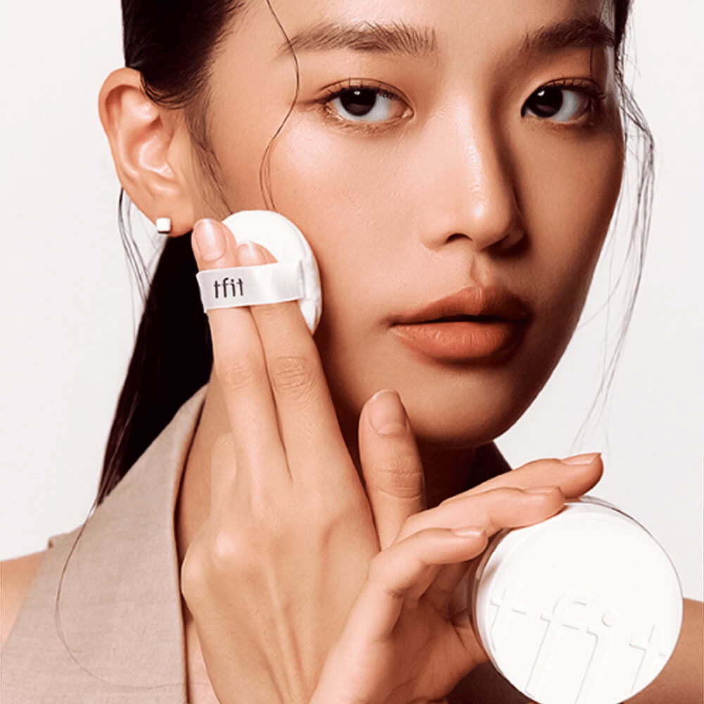 Mujer aplica TFIT Translucent Set Finishing Powder #02 Skin Beige con un puff, sostiene un frasco de polvo blanco con el logo de TFIT.