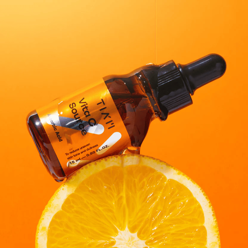 TIA'M Vita C Source-botella colocada contra una naranja y un fondo naranja que simboliza la frescura y el efecto antioxidante de la vitamina C.