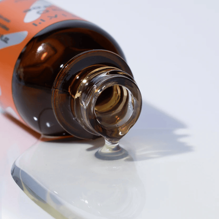 Närbild på TIA'M Vita C Source-serum som rinner ur en brun glasflaska. Serumets klara formula framhäver dess koncentrerade C-vitamininnehåll för en strålande hud.