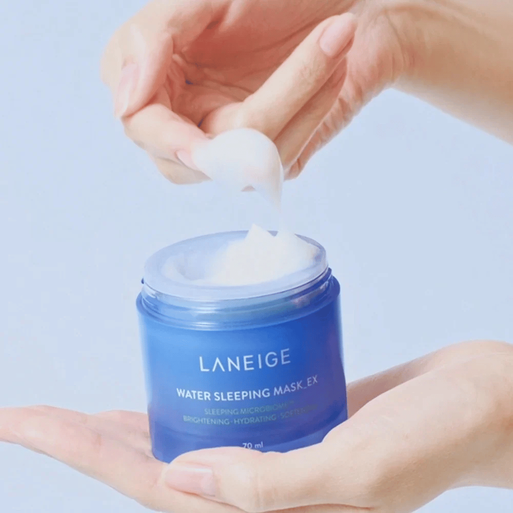 Una mano saca LANEIGE Water Sleeping Mask de un tarro azul, con enfoque en la consistencia gelatinosa contra un fondo azul claro.