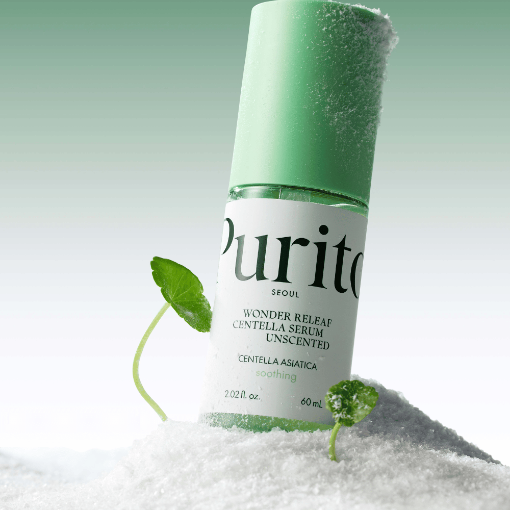 Botella con Purito Centella Serum está en la nieve, se ven hojas verdes, contra un suave fondo verde.