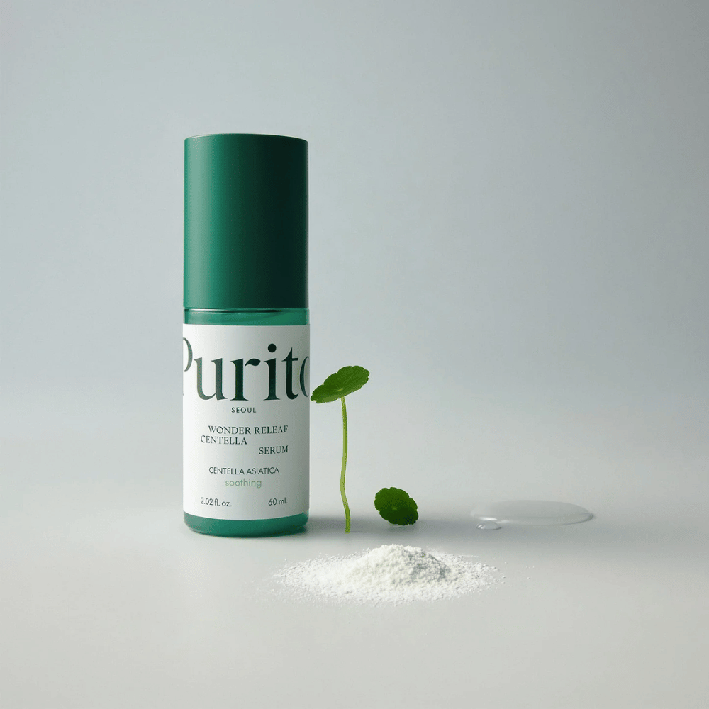 Botella verde de Purito Wonder Releaf Centella Serum 60 ml sobre una base blanca, rodeada de hojas de centella, una gota de suero transparente y un pequeño polvo blanco.