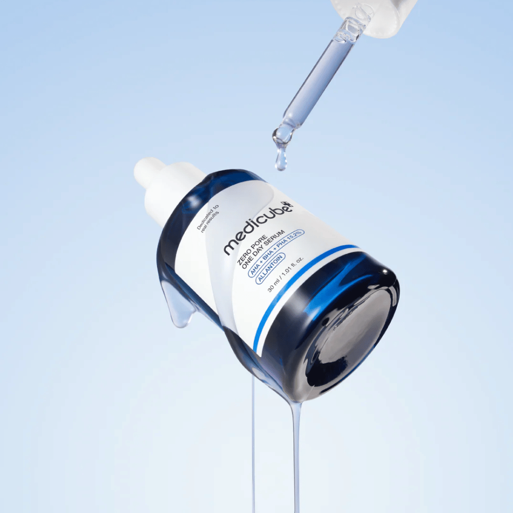 Botella de Medicube Zero Pore One Day Serum con pipeta y gotas de suero fluyendo sobre un fondo azul claro.
