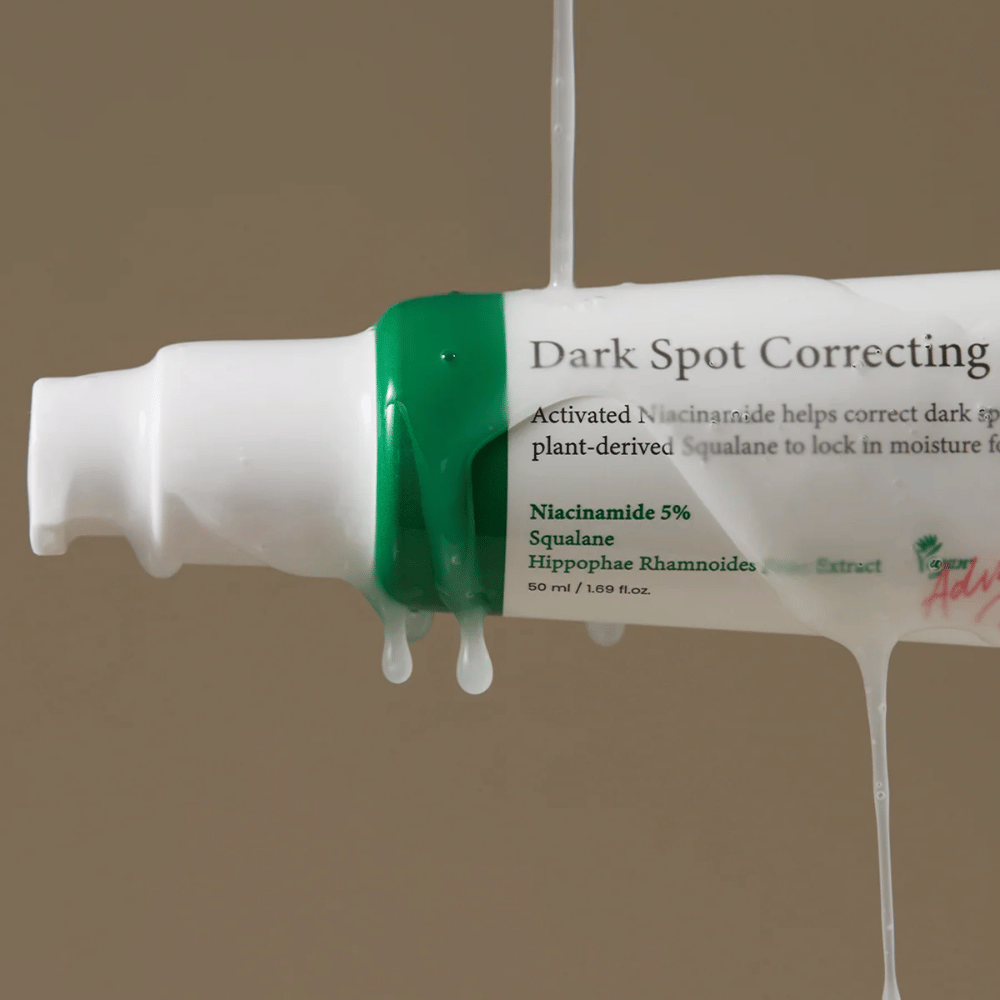 Primer plano de una botella con bomba de Axis-Y Dark Spot Correcting Glow Serum con empaque blanco y tapa verde, cubierta de líquido transparente corriendo.