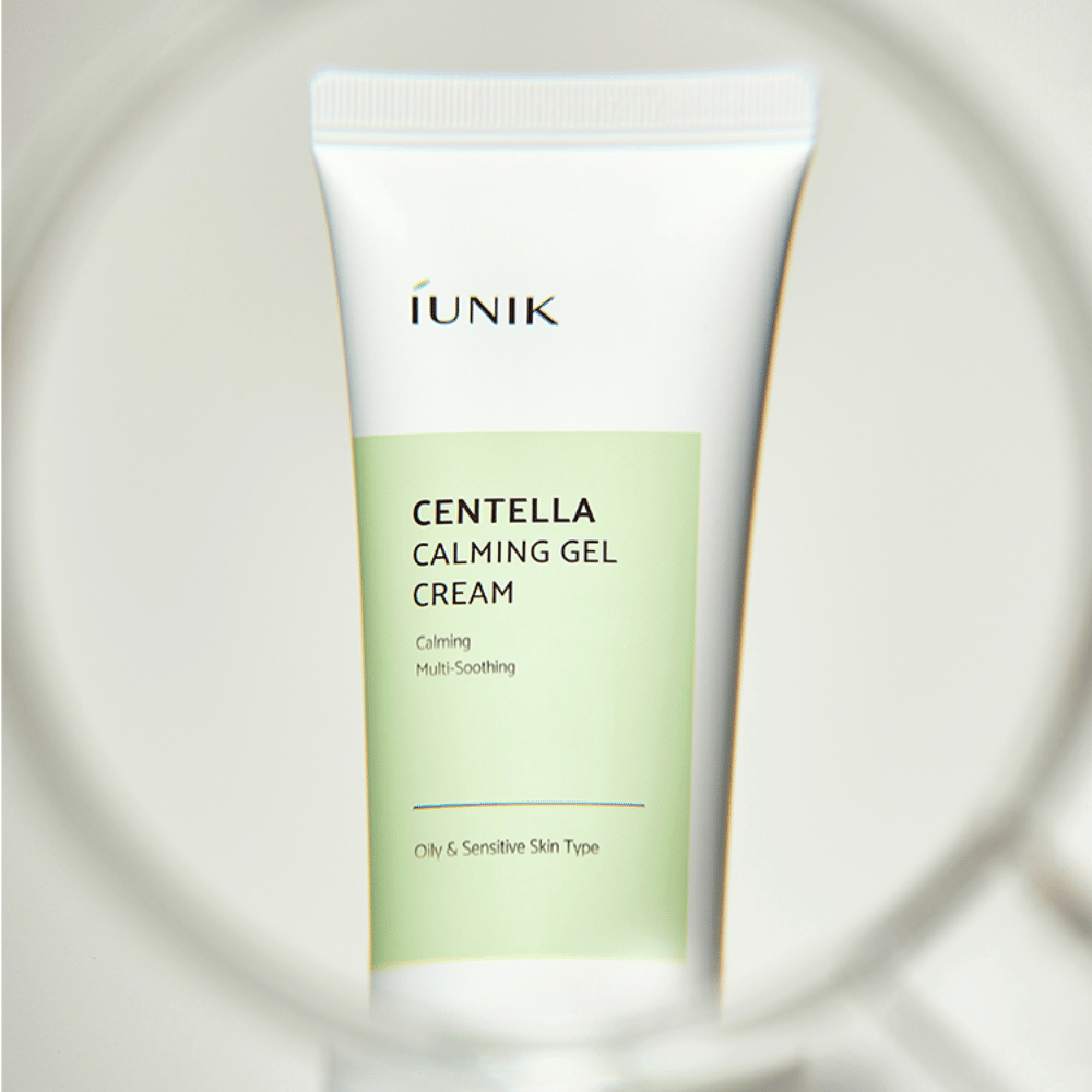 Un tubo iUNIK Centella Calming Gel Cream con diseño blanco y verde claro está de pie, visto a través de un marco redondo similar a una lupa.