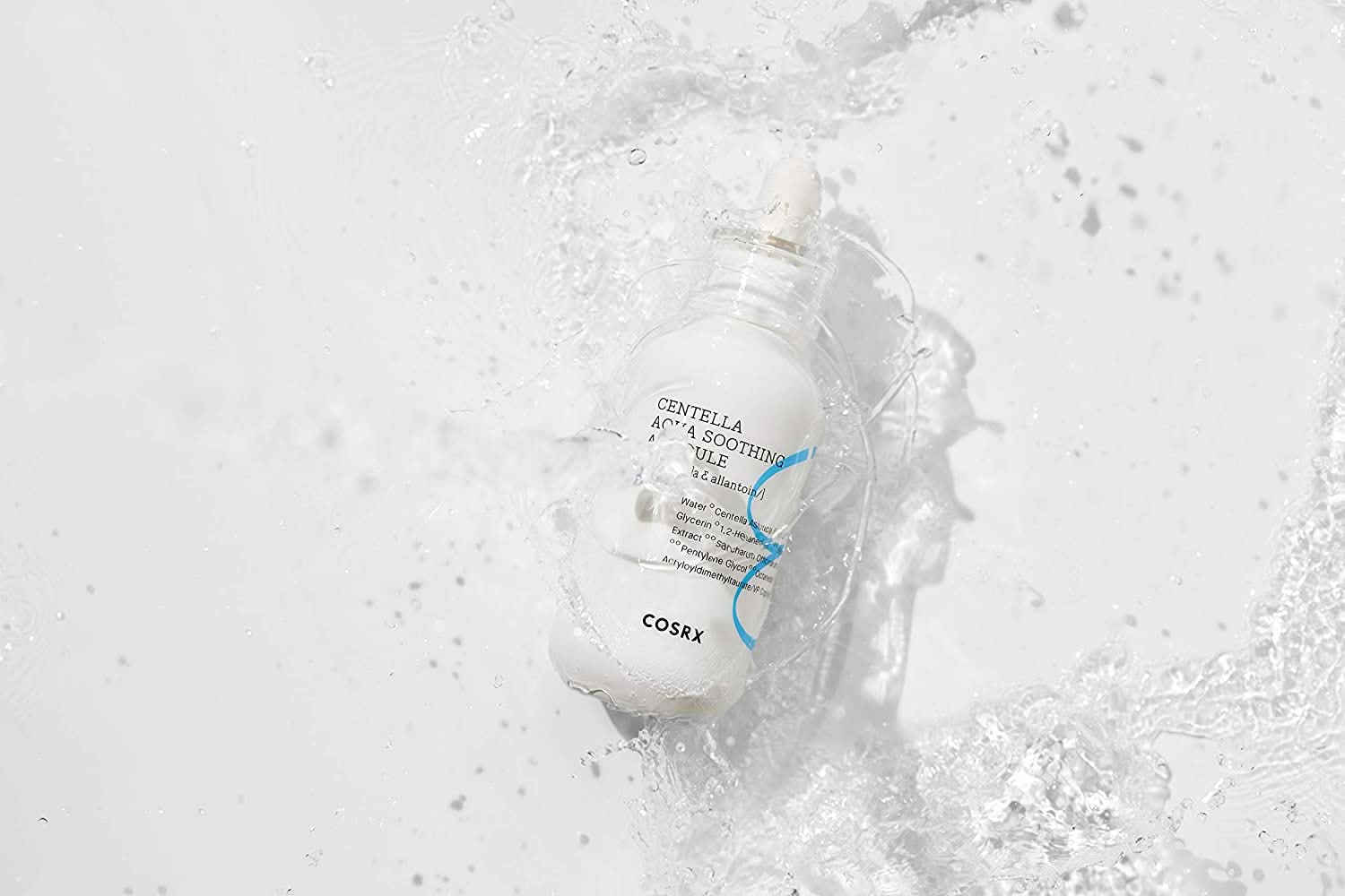 Una botella COSRX Centella Aqua Soothing Ampoule 40ml que salpica sobre una superficie blanca, reduce el enrojecimiento y proporciona hidratación calmante.