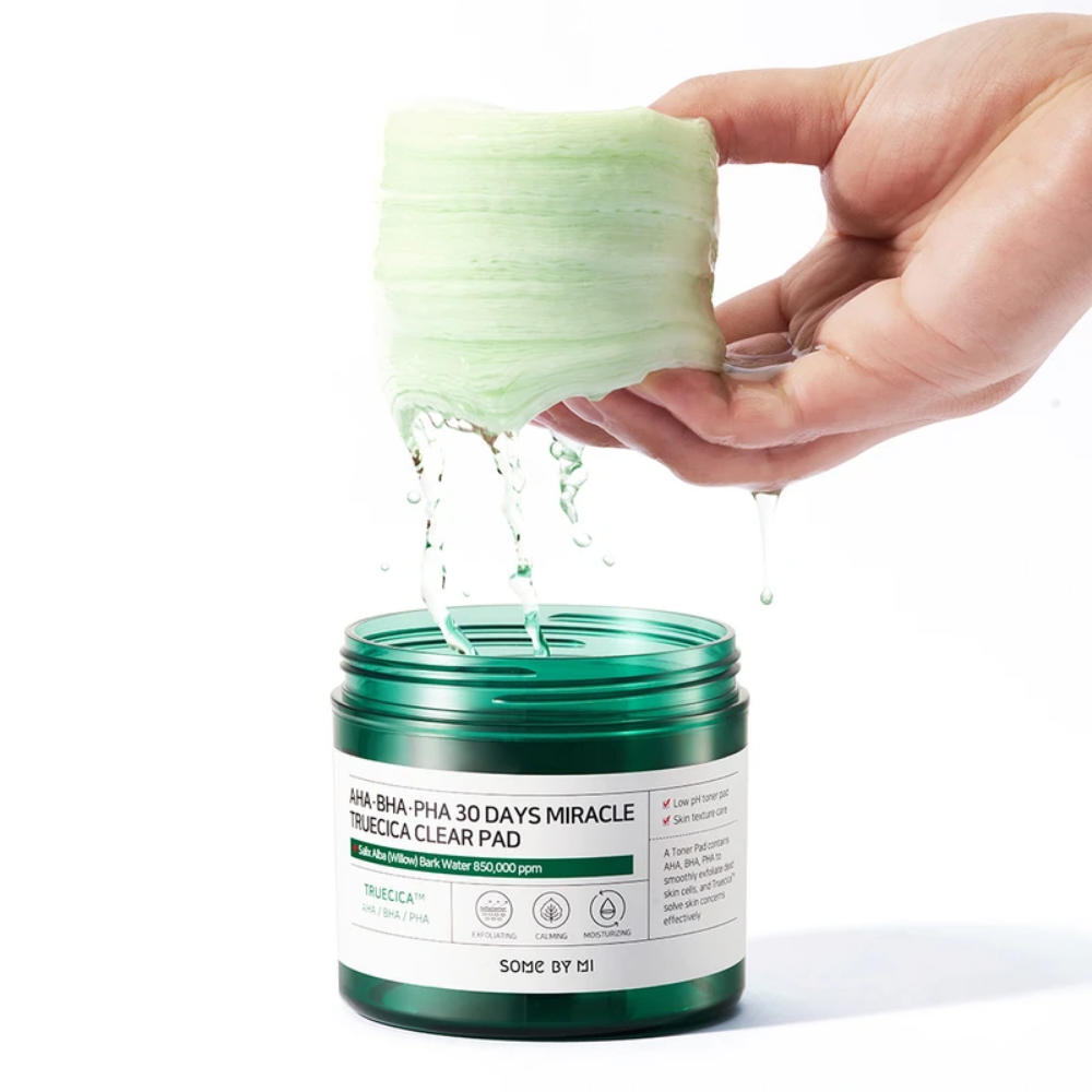 Una mano sostiene un líquido verde en un frasco para el tratamiento de 70 uds de brotes de acné de SOME BY MI:s AHA, BHA, PHA 30 Days Miracle Truecica Clear Pad.