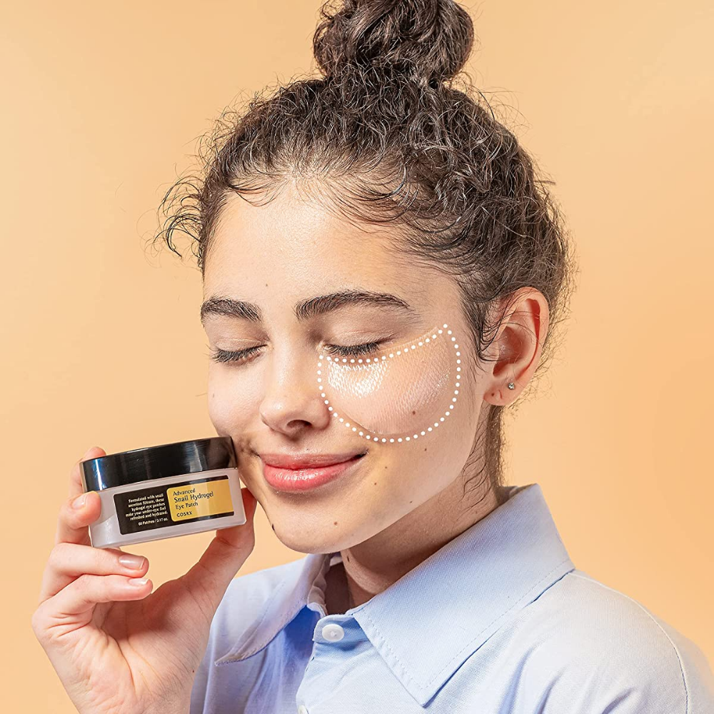 Una mujer que sostiene un tarro COSRX Advanced Snail Hydrogel Eye Patch 60 uds de crema facial.