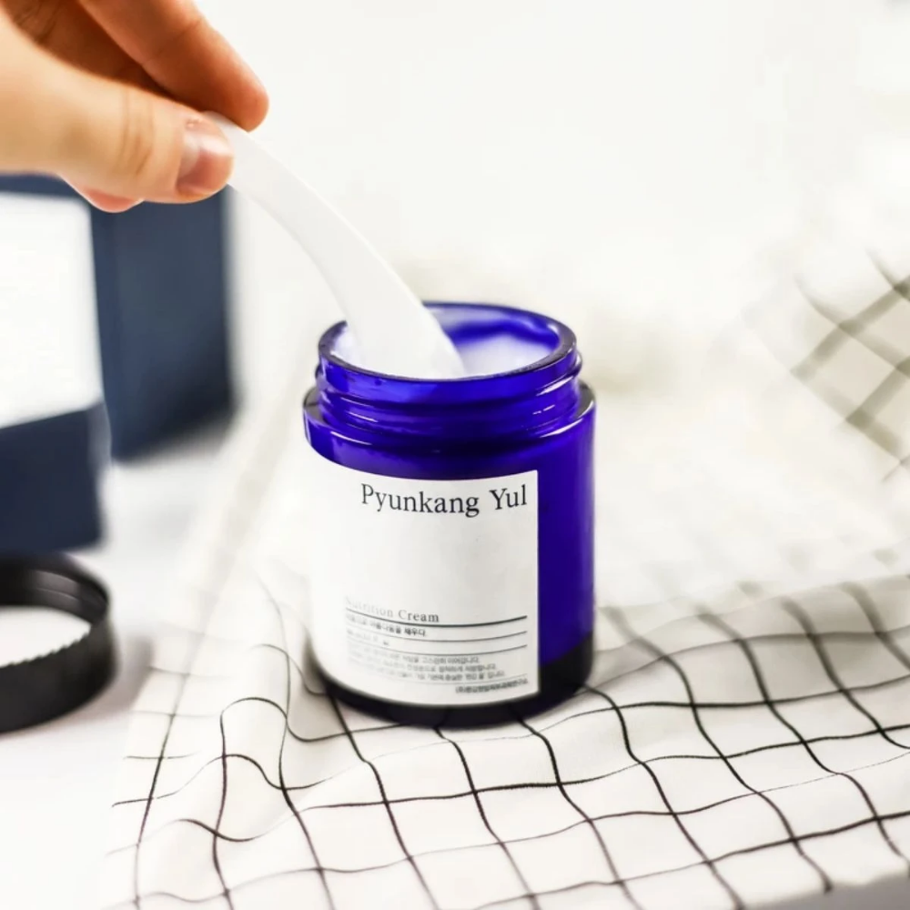 Una persona usa un tarro Pyunkang Yul Nutrition Cream 100ml sobre una mesa.