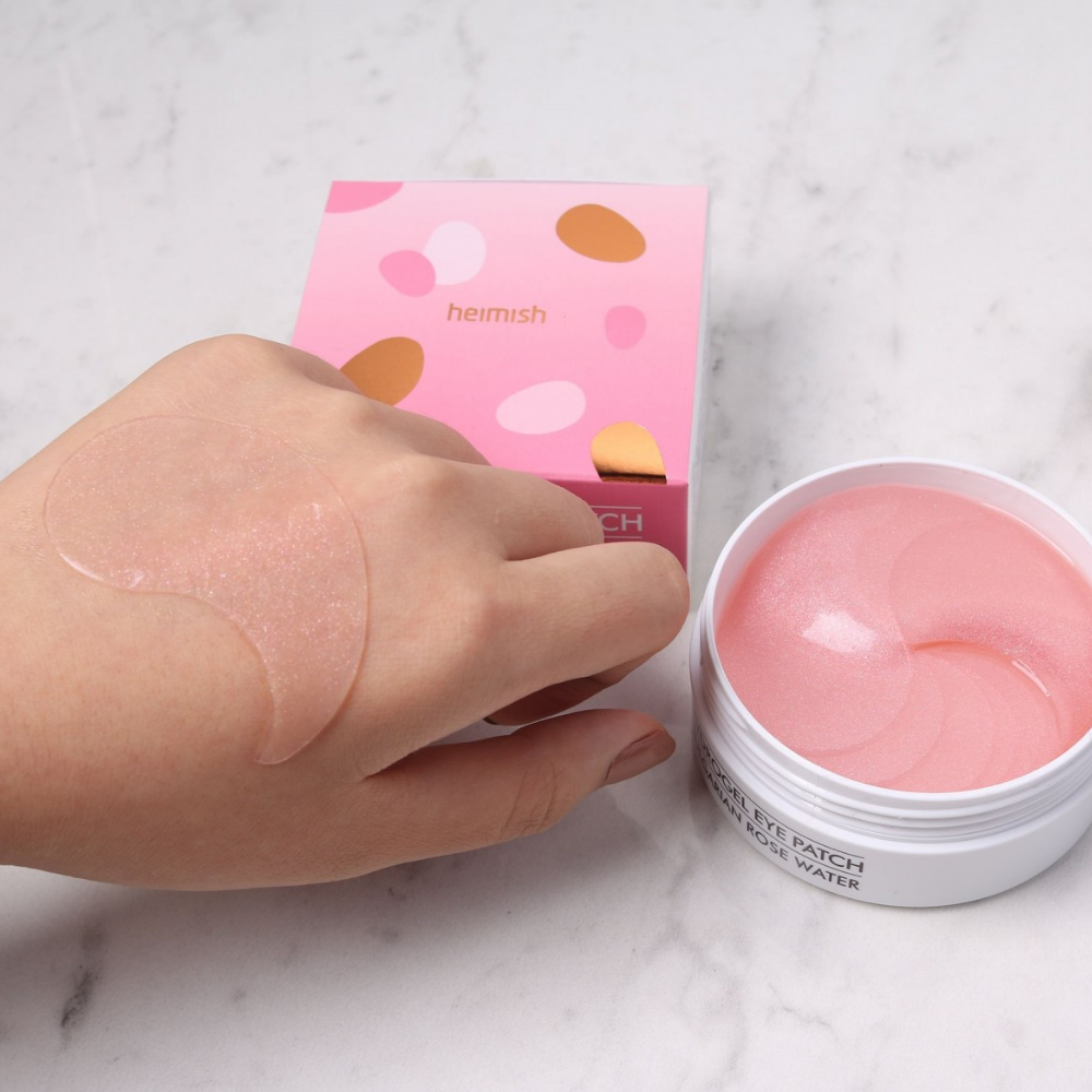 Una mano que sostiene un rosa Bulgarian Rose Hydrogel Eye Patch 60st de heimish y aplica una máscara para ojos.