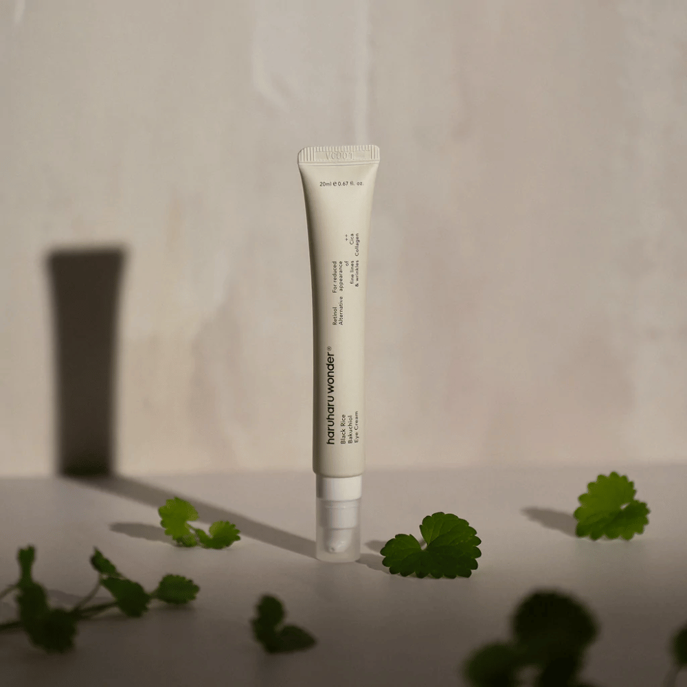 Un tubo Haruharu Wonder Black Rice Bakuchiol Eye Cream 20ml rodeado de hojas verdes, enfocado en la visibilidad de arrugas y líneas finas.