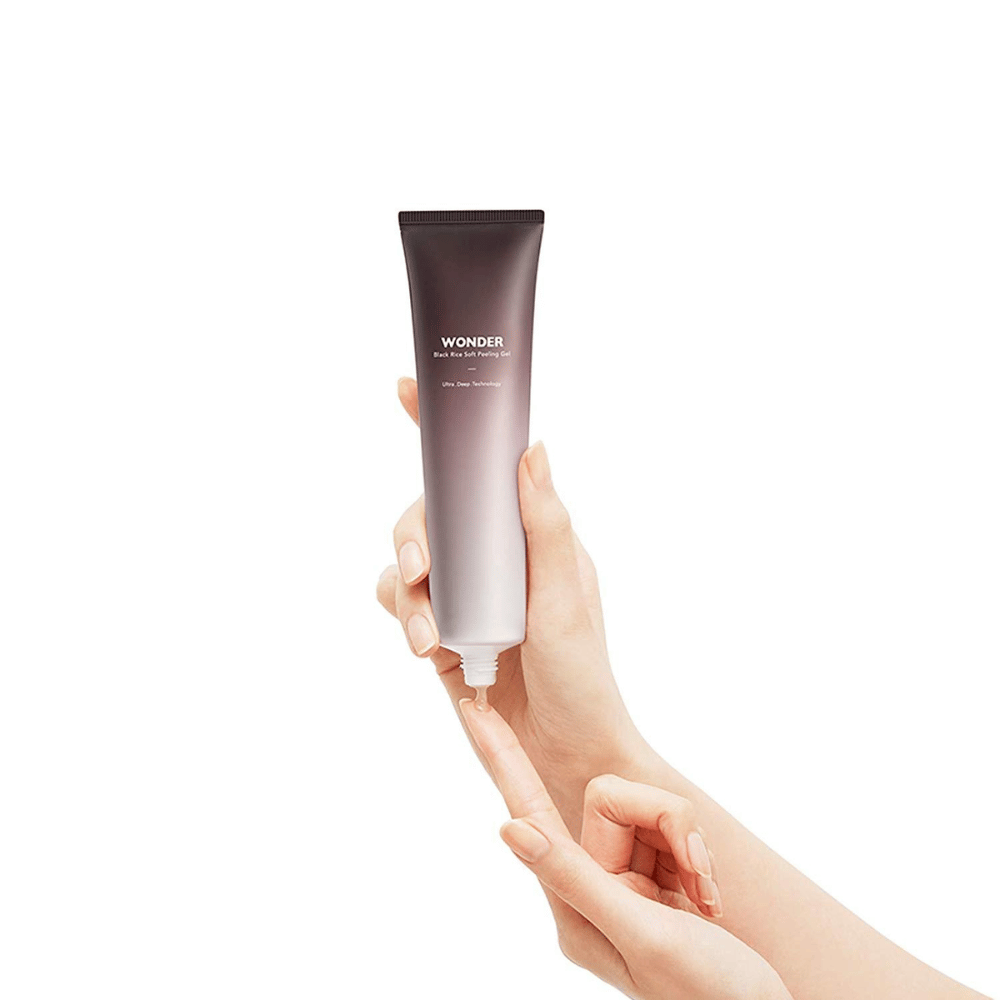 La mano de una mujer sosteniendo un tubo Haruhuru Wonders Black Rice Soft Peeling Gel 100 ml sobre un fondo blanco.