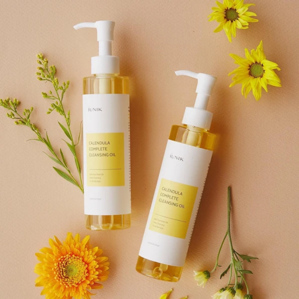 Dos botellas iUNIK Calendula Complete Cleansing Oil 200ml con flores amarillas sobre fondo beige, infundidas con aceite vegetal.