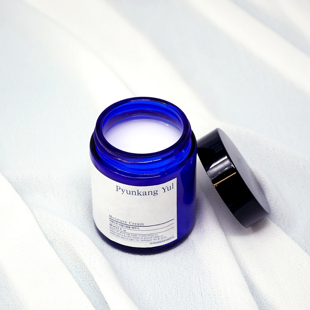 Un tarro azul con tapa que se encuentra sobre un paño blanco mostrando las propiedades hidratantes de Pyunkang Yul's Moisture Cream 100ml.