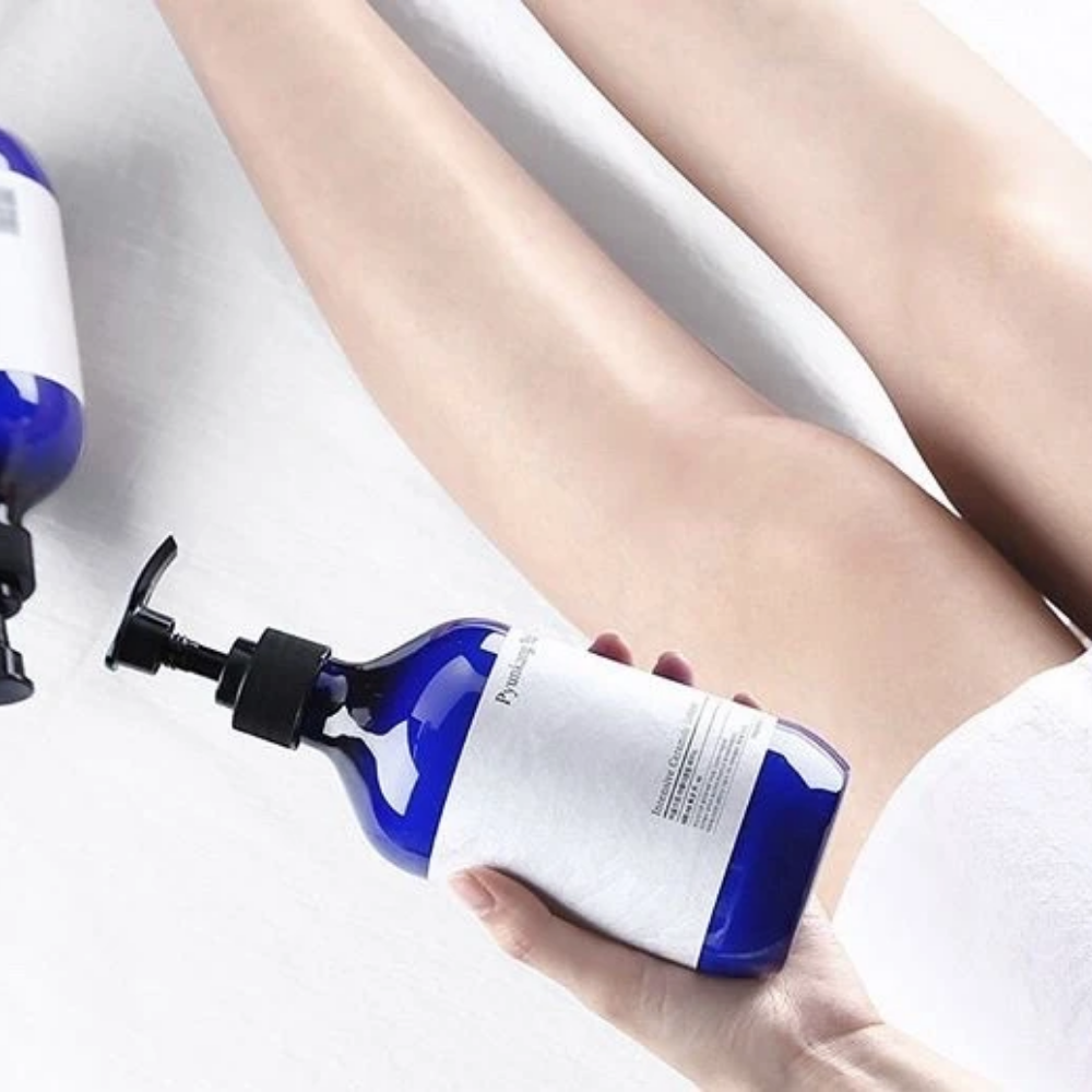 Una mujer que sostiene una botella Pyunkang Yul Intensive Ceramide Lotion 500ml junto a sus piernas.