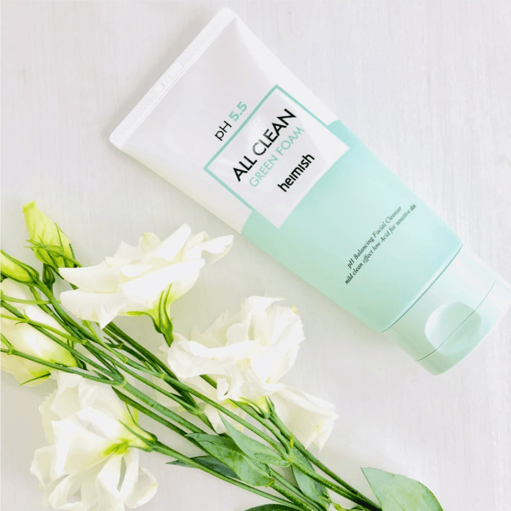 Un tubo heimish All Clean Green Foam 150ml al lado de flores blancas.